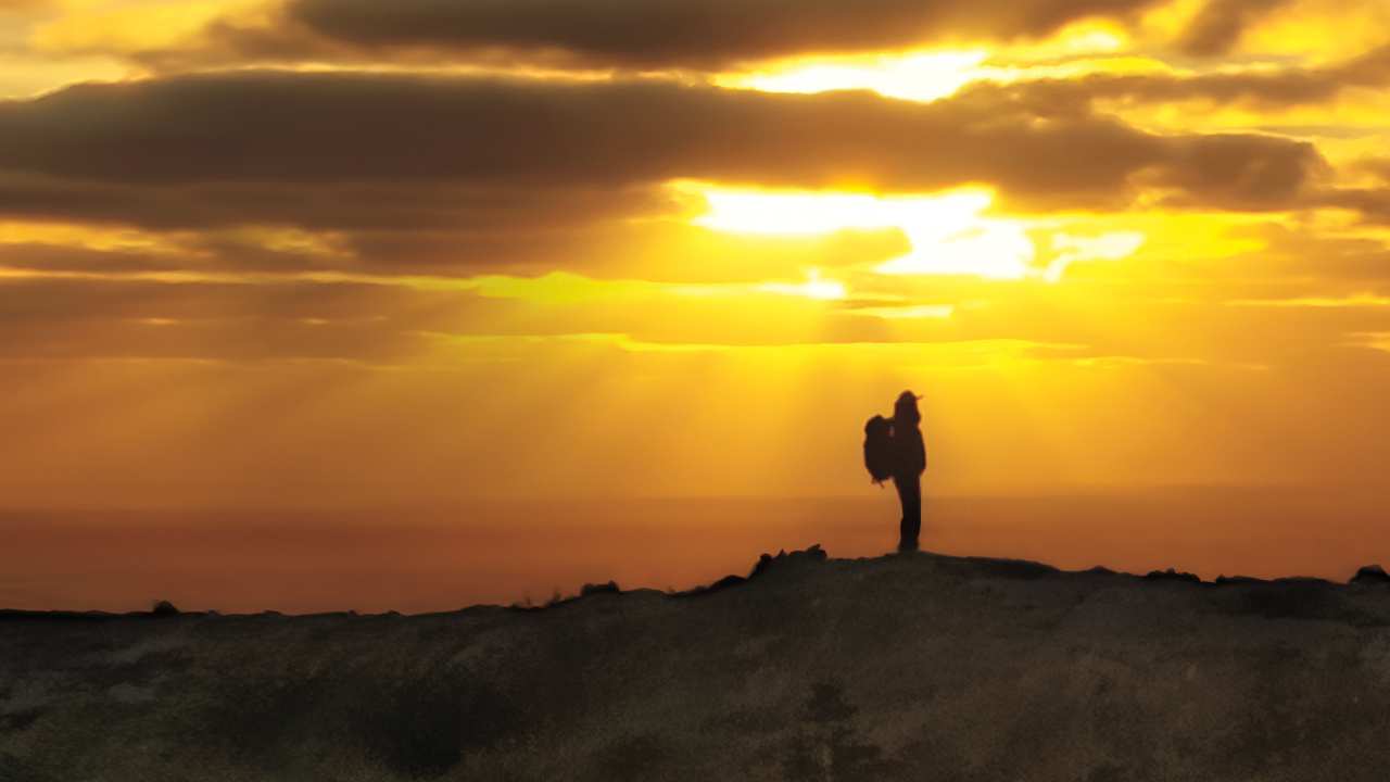 a woman with a backpack standing as the sun rises